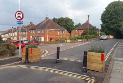 Planters and bollard across a road depicting a modal filter that allows pedestrians and cyclists access, but prevents come vehicles