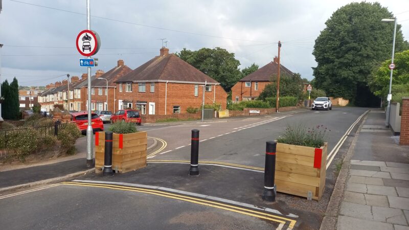 Planters and bollard across a road depicting a modal filter that allows pedestrians and cyclists access, but prevents come vehicles