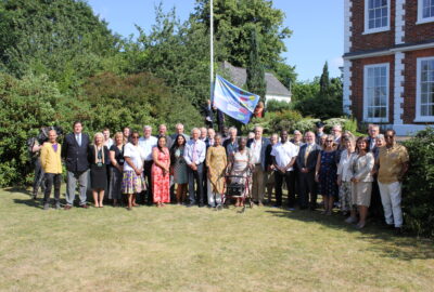 A large gathering of people met at County Hall to raise the Windrush Devon flag. Crowd stood by the flagpole, with the Windrush Flag
