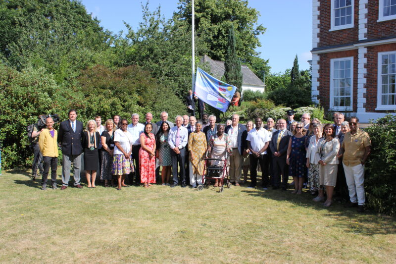 A large gathering of people met at County Hall to raise the Windrush Devon flag. Crowd stood by the flagpole, with the Windrush Flag
