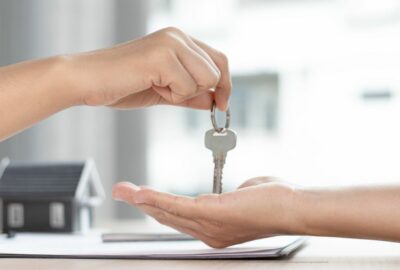 A person handing over some keys to someone else. Only their forearms and hands, and a key dangling from a finger, can be seen.