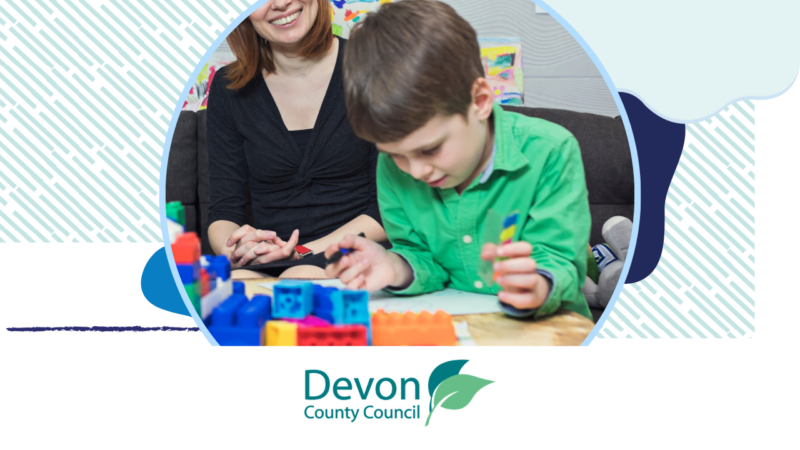 A young boy playing with colourful building blocks whilst an adult looks on.
