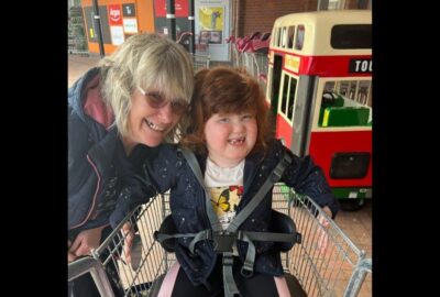 Debbie and Bo smiling at the camera. Bo is sat in a supermarket trolley