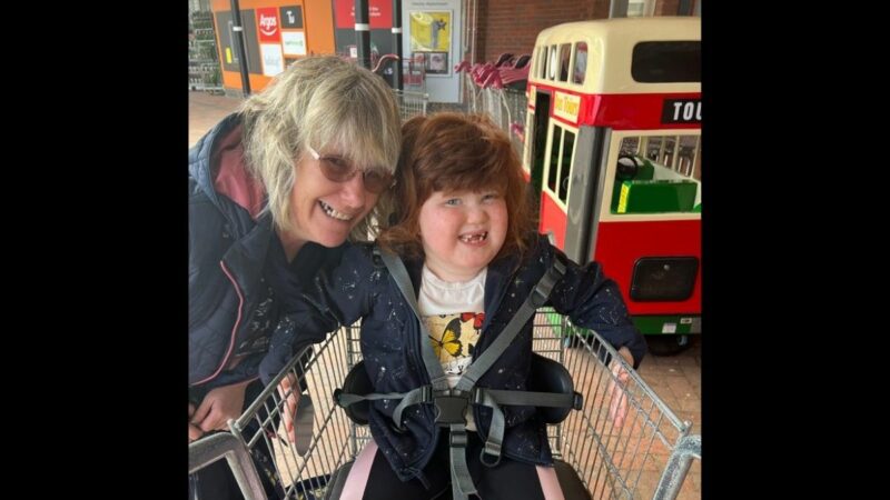 Debbie and Bo smiling at the camera. Bo is sat in a supermarket trolley