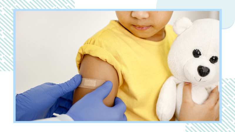 A young child cuddling a teddy has a plaster put on their arm