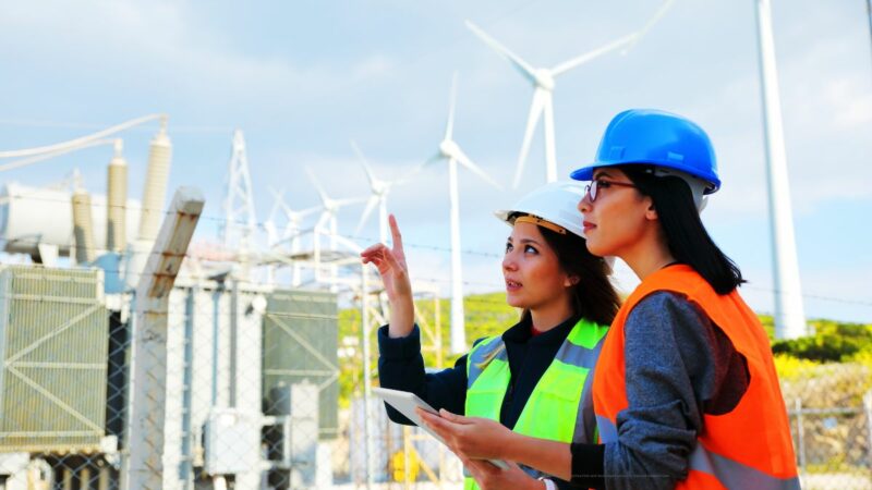 Two workers wearing hard hats stood outside looking at some wind turbine-related technology