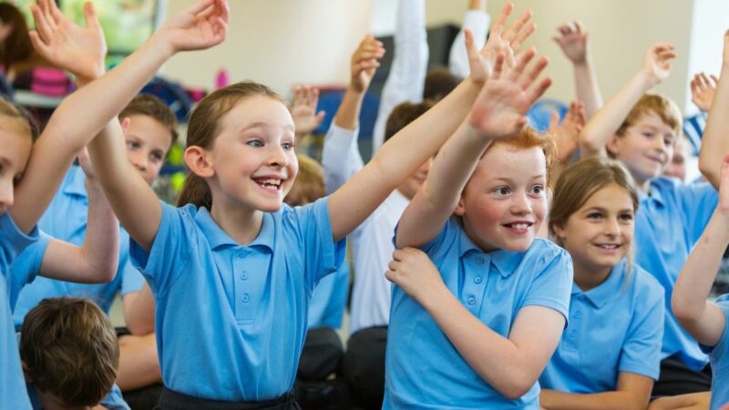 A primary school class of pupils with their hands up waiting to speak