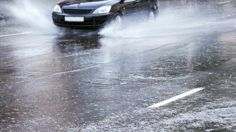 A car driving through rain with water spraying from the tyres