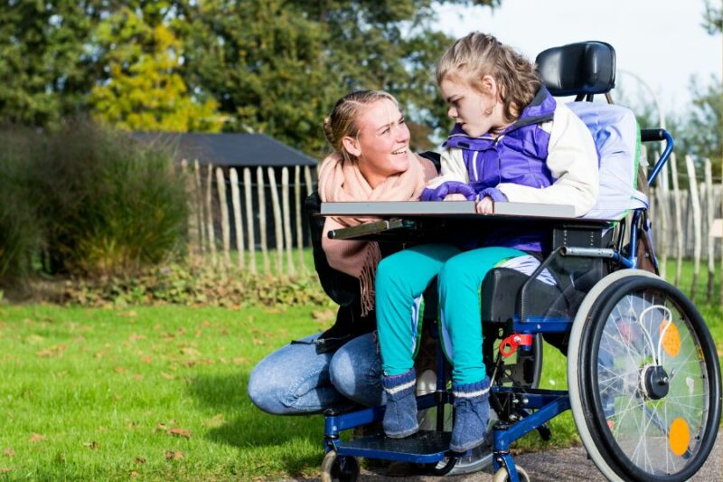 Woman kneeling next to child in wheelchair