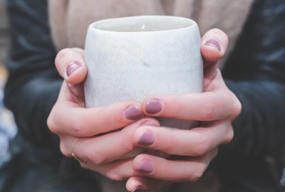 Two hands held around a mug of something warm to drink.