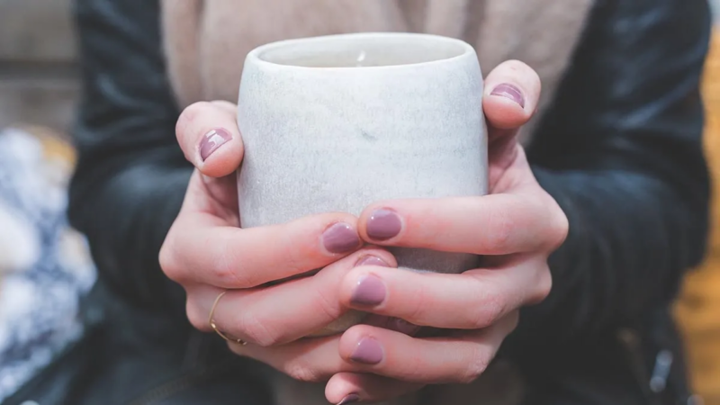 Two hands held around a mug of something warm to drink.