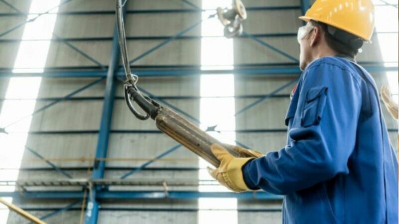 A worker in blue overalls and hard hat working in a factory