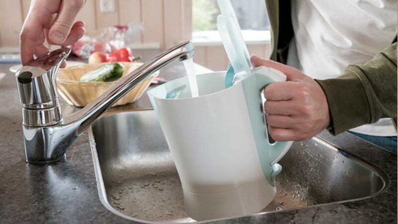 A person filling the kettle with water from the tap in a kitchen
