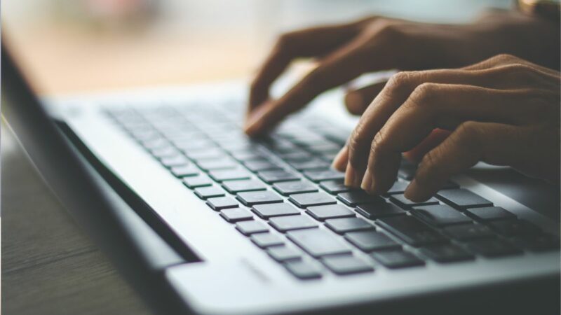 A person typing on a laptop. Only their hands are visible, on the keyboard of the laptop