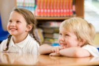 two young children sat at a school table smiling