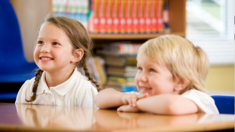 two young children sat at a school table smiling