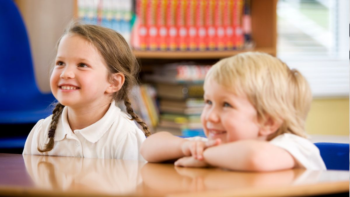 two young children sat at a school table smiling