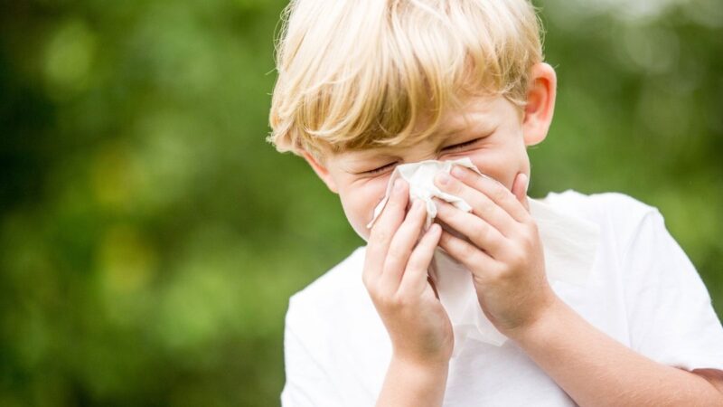 A young boy, outside, sneezing into a tissue