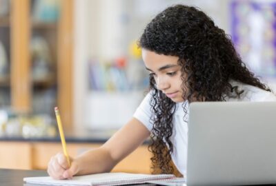 Child writing with a laptop in front of her
