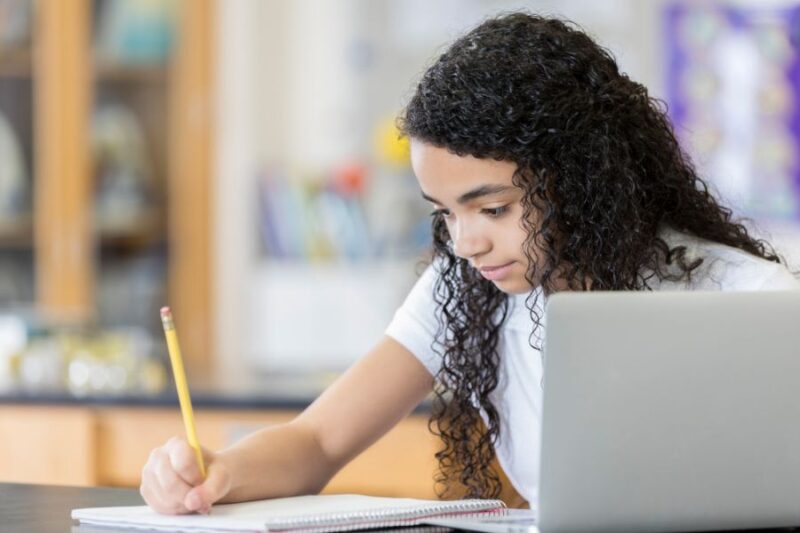Child writing with a laptop in front of her
