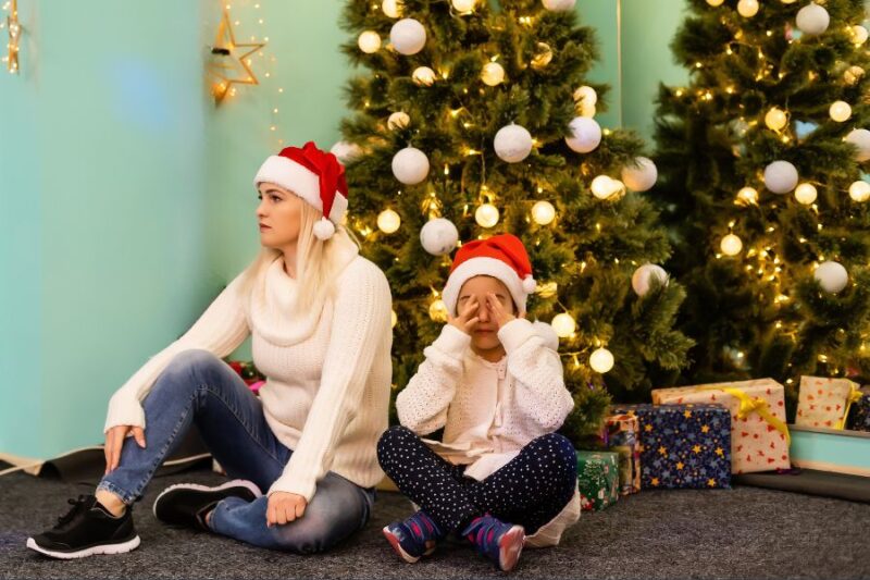 Mother and child sat under Christmas tree looking stressed