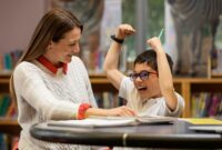 one to one support from an adult with a vulnerable child. The two are sat at a desk with a book in front of them. The child is laughing and smiling.