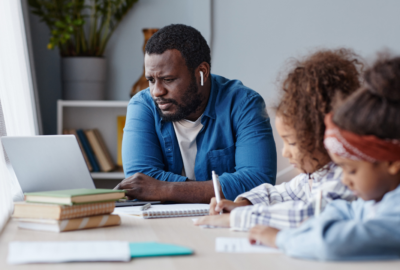 Father sat at laptop watching something alongside two young girls