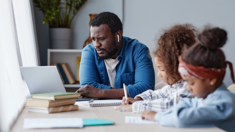 Father sat at laptop watching something alongside two young girls