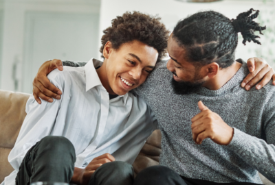 Father with his arm around son sat on sofa