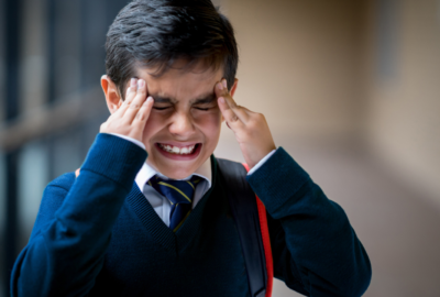 Boy in school uniform holding head looking stressed