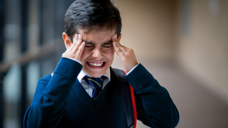 Boy in school uniform holding head looking stressed