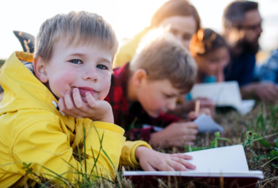 Child in a group lying on grass with a notepad