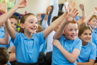 Happy children in a classroom with their arms raised in the air