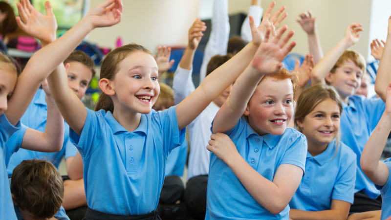 Happy children in a classroom with their arms raised in the air