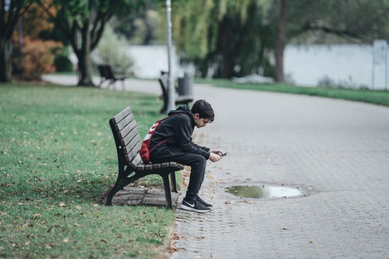 Teenage boy sat on a bench looking at phone