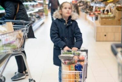 A little girl pushing a child's trolley in a supermarket with food in the shopping trolley