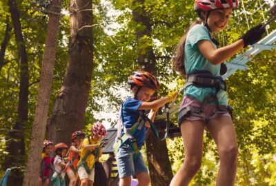 A line of children climbing, with harnesses, up in the tree tops, along a trail