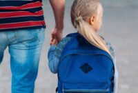 A young girl holding her dad's hand walking to school on her first day
