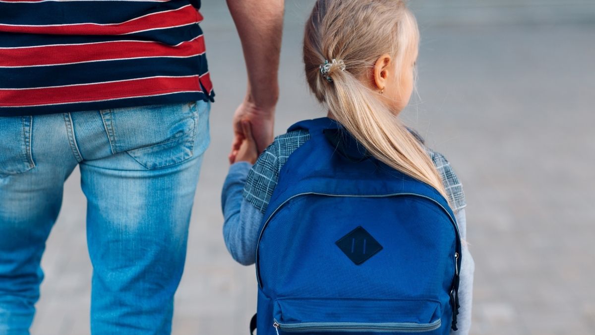 A young girl holding her dad's hand walking to school on her first day