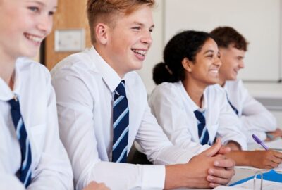 A row of teenagers sat in their class room all looking ahead and smiling, wearing uniform