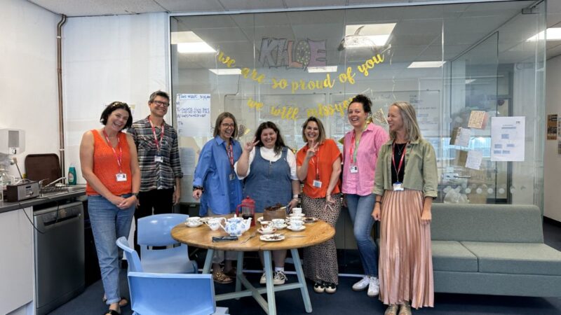 Khloe and the H2O team at Petroc College. The group are smiling and stood behind a desk with celebratory snacks