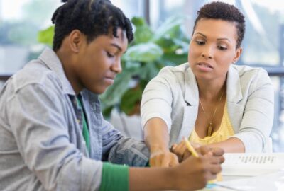 A teenager at home with their mum sat at a table looking at a school book.