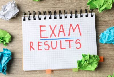 The words 'exam results' written in a note pad, with screwed up pieces of paper on the desk around the notepad.