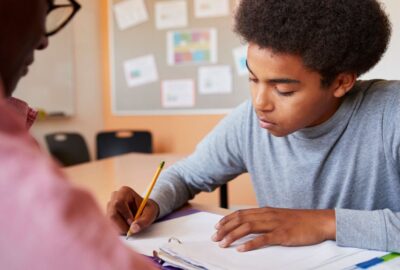 Boy working with a teacher one-to-one. Boy writing in his book