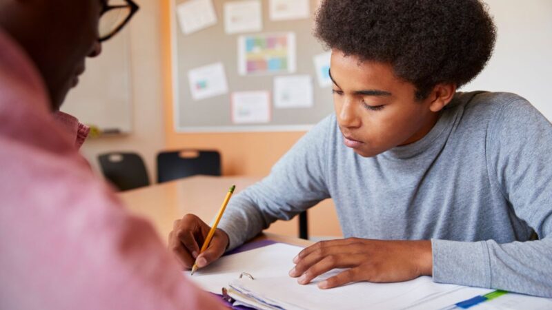 Boy working with a teacher one-to-one. Boy writing in his book