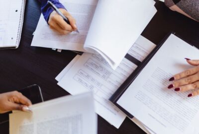 People working together in a meeting/ Photo shows different people's hands writing on notepads at a meeting table