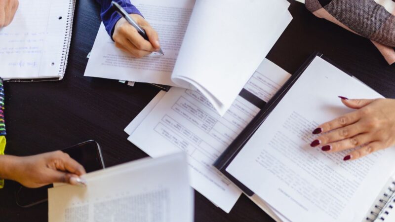 People working together in a meeting/ Photo shows different people's hands writing on notepads at a meeting table