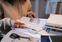 Young person sat at her desk at home studying, looking through a form.