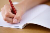 A young pupil writing in their book. Only their hands and a pencil and exercise book in the picture