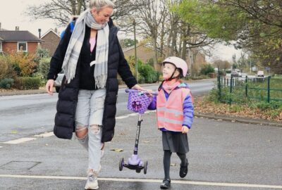 Young girl in hi-vis crossing the road with her mum